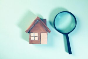 Wooden house model next to a magnifying glass, representing property protection strategies after a home inspection.